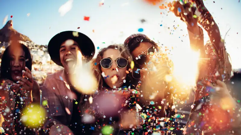 Eine Gruppe Feiernde mit Konfetti und Luftschlangen vor einem blauen Himmel