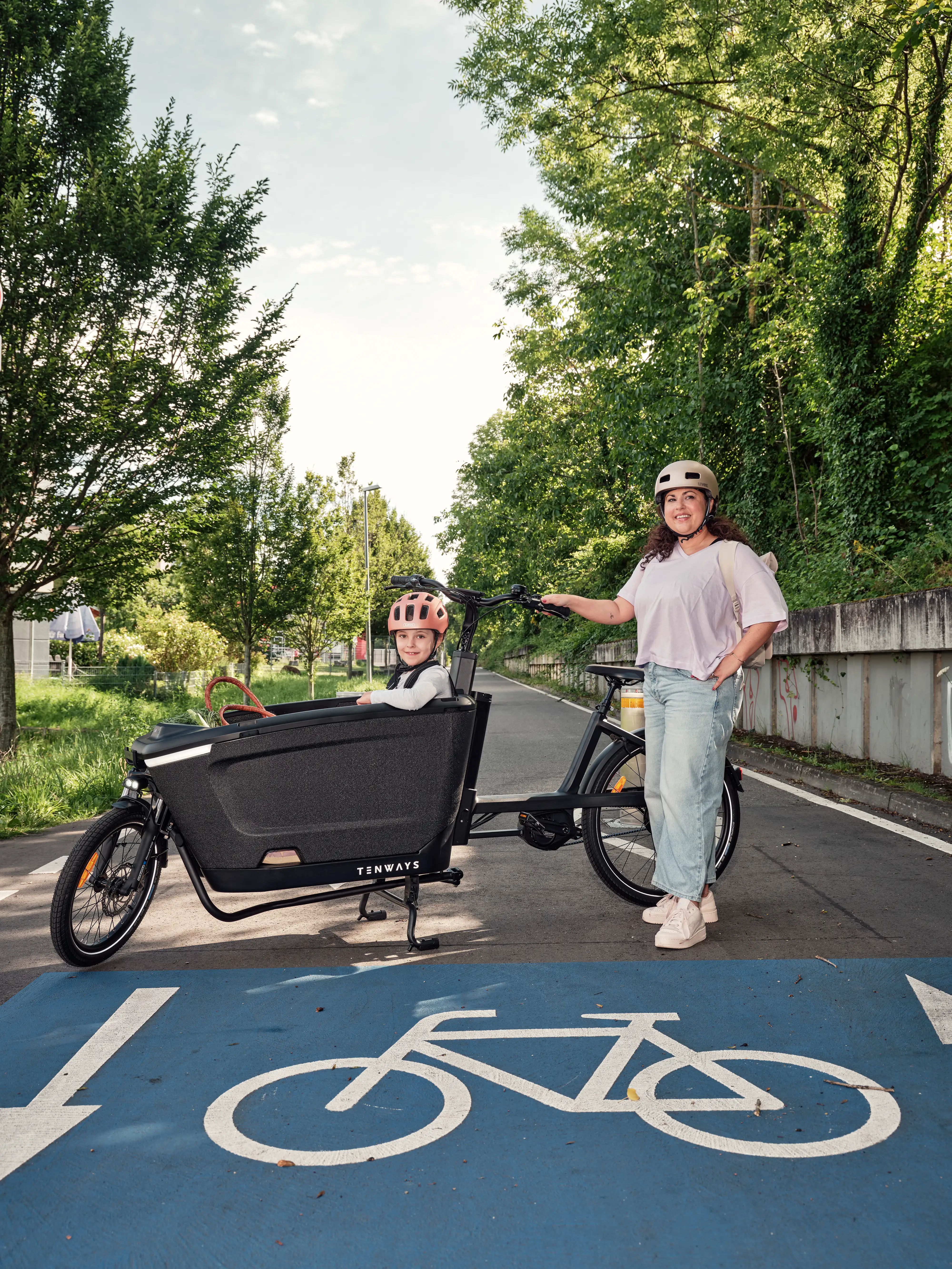 JobRadlerin posiert stolz neben ihrem Lastenrad mit Kind auf der Fahrradstraße